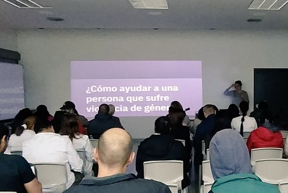 Aula durante un curso, con el público de espaldas y una diapositiva proyectada que pregunta cómo ayudar a una persona que sufre violencia de género